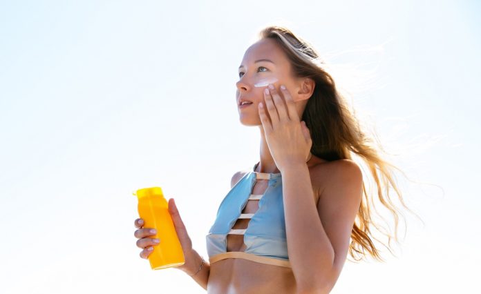 Slim woman applying sunscreen for her face, on the beach
