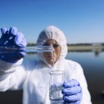 Ecologist sampling water from the river with test tube.